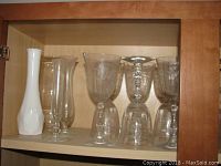 Cabinet shelf showing four bud vases including one opaque white and three clear glass, some etched floral design observed.