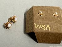 Both pairs of earrings, pearl star pair on branded card and opal pair off card