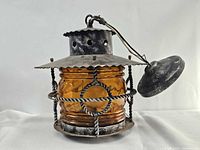 Front view showing amber glass globe, metal cage, hinged lid and hanging wire