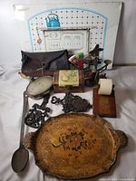 Group shot of all antique items including tole tray, wall panel, cast iron pieces, mirror, spoon, leather pouch, box and note holder
