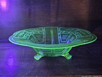 Side view of glowing green uranium glass bowl showing etched pattern and three feet