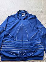 Front view of blue Adidas track jacket showing Trefoil outline and stripes