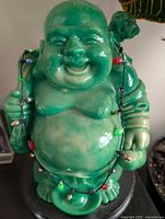 Front view of green Laughing Buddha statue with string lights draped