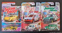 Front view of three sealed Matchbox candy-branded cars: Sugar Daddy sports car, Tootsie Roll Pop Volkswagen Caddy Delivery, Junior Mints Austin Mini Van