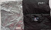 Grey t-shirt in plastic and two black t-shirts folded