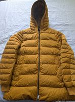 Front view of mustard yellow Geox hooded puffer jacket laid flat showing quilting, zipper and cuffs
