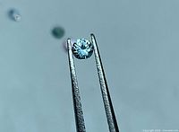 Loose round sapphire held in tweezers