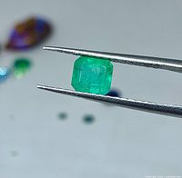 Emerald-cut green gemstone held by tweezers