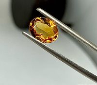 Close-up of oval faceted golden citrine gemstone held in tweezers