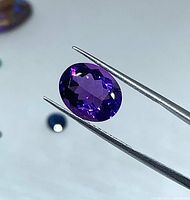 Oval purple amethyst held by tweezers showing facet pattern and clarity