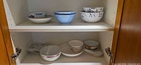 two-shelf cabinet showing full lot of bowls, plates and spoons