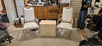 Front view of two light-wood upholstered arm chairs flanking matching two-drawer side table