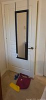 Over-the-door mirror hanging on white door with workout items on floor