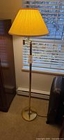 Full view of brass-tone floor lamp standing on carpet with shade illuminated