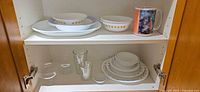 Cabinet view with Corelle stack, clear glasses, oval platter, oval bowls, mug