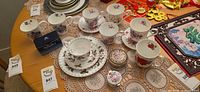 Group view of pill box, multiple floral teacups, holly cup-saucer-plate set