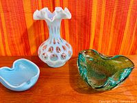 White opalescent hobnail vase, blue heart-shaped dish, green freeform bowl on wood surface, striped background