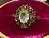 Close-up of ring showing ornate gold setting and green glass stone