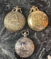 All three pocket watches showing front covers with train, steam pumper and fishing scenes