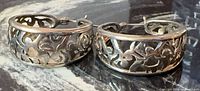 Pair of sterling silver cutout scroll hoop earrings on dark surface