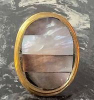 Front view of oval ring showing three mother of pearl stripes in brass bezel