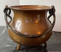 Front view of copper cauldron showing iron handle and three legs