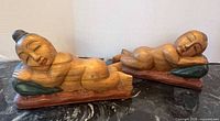 Pair of reclining carved wood Asian figures on marble surface