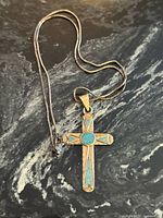 Cross pendant on snake chain displayed on dark stone background