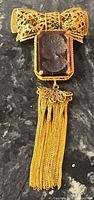 Front view showing bow, purple intaglio cameo, tassel