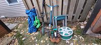 All items leaned against fence: hose reel, chairs, tools, camp chair, hanging basket