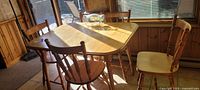 Dining table with four of the five chairs around it, sunlight highlighting light maple finish