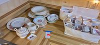 Overview of assorted mismatched china pieces including stacked plates, saucers, teacups in storage caddy, sugar bowl, creamer and small dish