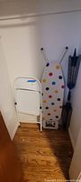Ironing board with polka-dot cover and folding chair in closet