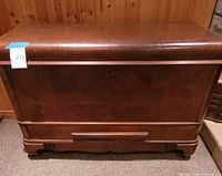 Front view of wooden trunk showing overall form, veneer finish and base drawer