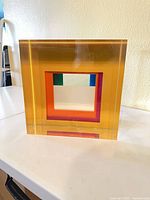 Front view showing transparent amber block with concentric square aperture and color plates