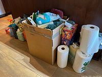 Overall lot showing box full of cleaners, detergents, sprays, cloths, brushes plus paper towel rolls and tissue boxes