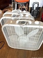 Three white Lasko box fans angled front view showing grilles, handles, cords