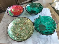 Overhead view of four bowls: cloisonné floral, two green glass shells, multicolor pottery