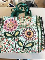 Stack of laminated totes showing top bag with large stylised flowers, green straps visible