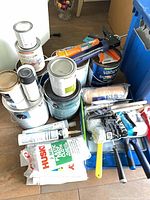 Overview of paint cans, caulk gun, roller covers and blue tote