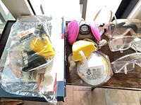 All PPE items on table, respirator with filters, goggles, gloves, N95 mask visible