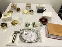 Assorted drain stoppers, tub spout, bidet sprayer kit laid out on table