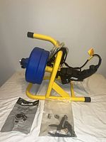 Side view of drain auger on yellow frame with blue drum, cable, drill motor, cutters bag and manual displayed