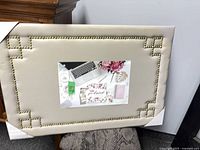 Front view showing taupe fabric, brass tack border, centre example photo, corner protectors on