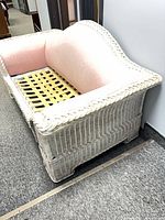Front angle of white wicker loveseat showing pink upholstered panels and missing seat cushion