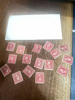 All 16 red 2-cent George Washington stamps spread on wood surface