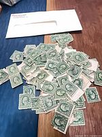Pile of green 1¢ Washington stamps next to envelope
