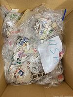 Open cardboard box showing several clear bags stuffed with loose stamps
