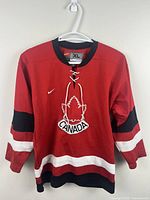 Front view of red Nike Team Canada jersey showing crest, stripes and lace-up collar