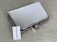 Front angled view of silver-tone clutch showing textured body, rhinestone frame and crystal clasp